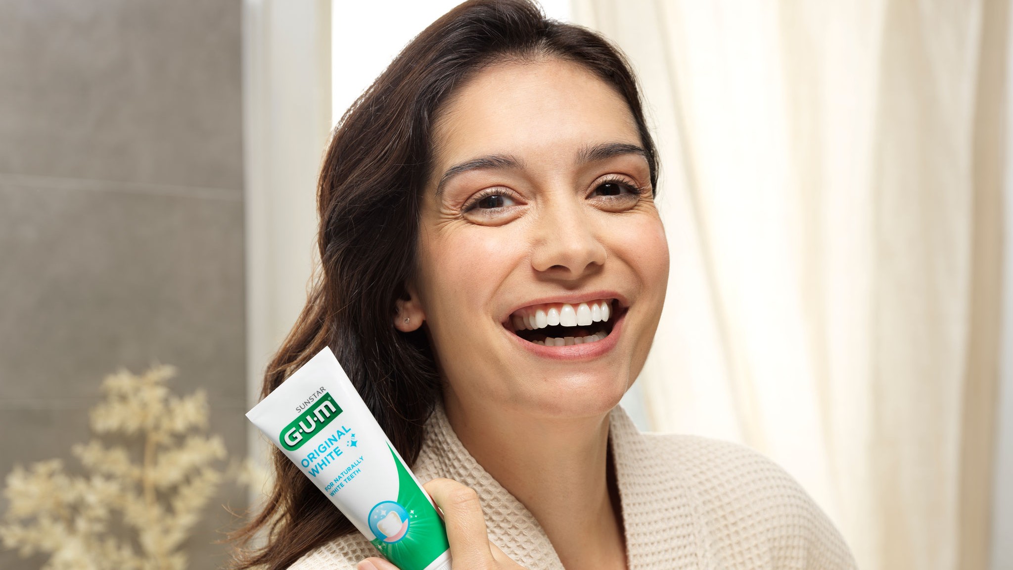 Woman holding toothpaste in bathrobe.